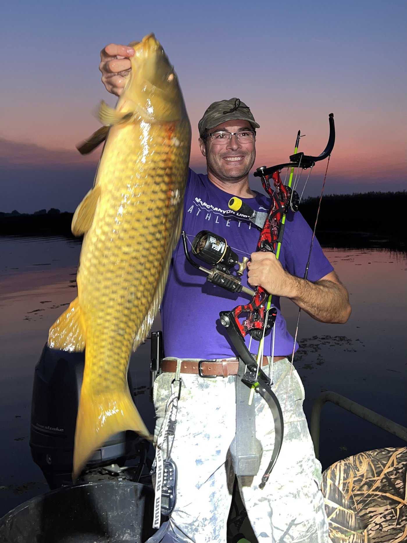 Rod holding a trophy carp at sunset, bow in hand