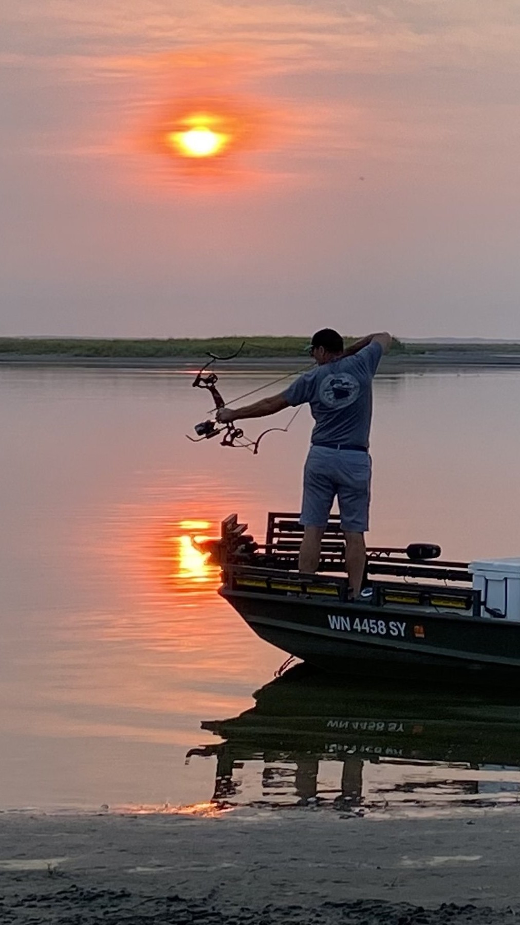 Bowfisherman at full draw on a SeaArk boat, sun rising behind him